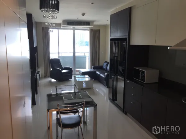 Condominium for rent in Bang Rak, Bangkok - Open-plan kitchen and living area with leather sofa, chandelier lighting and balcony glass doors.