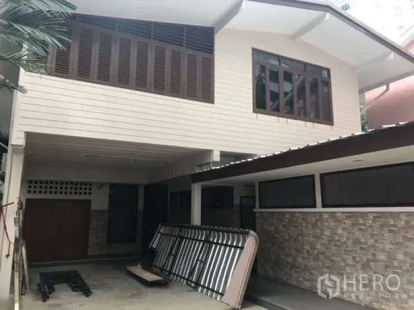 独立式住宅 出租在Watthana, Bangkok - 双层独栋房屋外观，带遮雨车位、木百叶与石纹墙面。