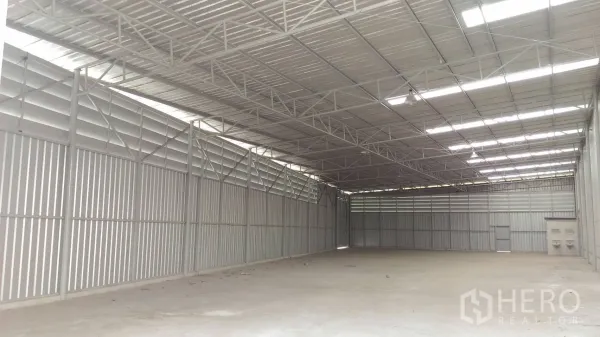Warehouse for rent in Lam Luk Ka, Pathum Thani - Spacious warehouse interior with steel trusses, louvered ventilation and skylights above a smooth concrete floor.