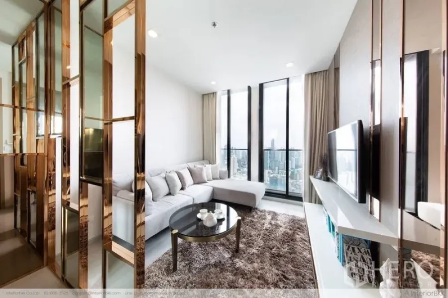 คอนโด ให้เช่าในPathum Wan, Bangkok - ห้องนั่งเล่นสว่างด้วยโซฟาเข้ามุม พรมขนฟู ผนังทีวี และหน้าต่างเต็มบานมองเห็นวิวสกายไลน์กรุงเทพฯ