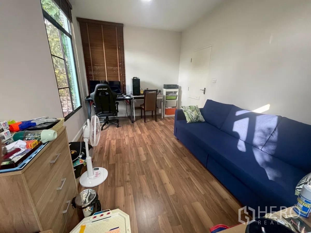 บ้าน ขายในBang Phli, Samut Prakan - ห้องอเนกประสงค์ชั้นล่าง โซฟาสีน้ำเงิน โต๊ะทำงาน พื้นไม้ และหน้าต่างมองสวน