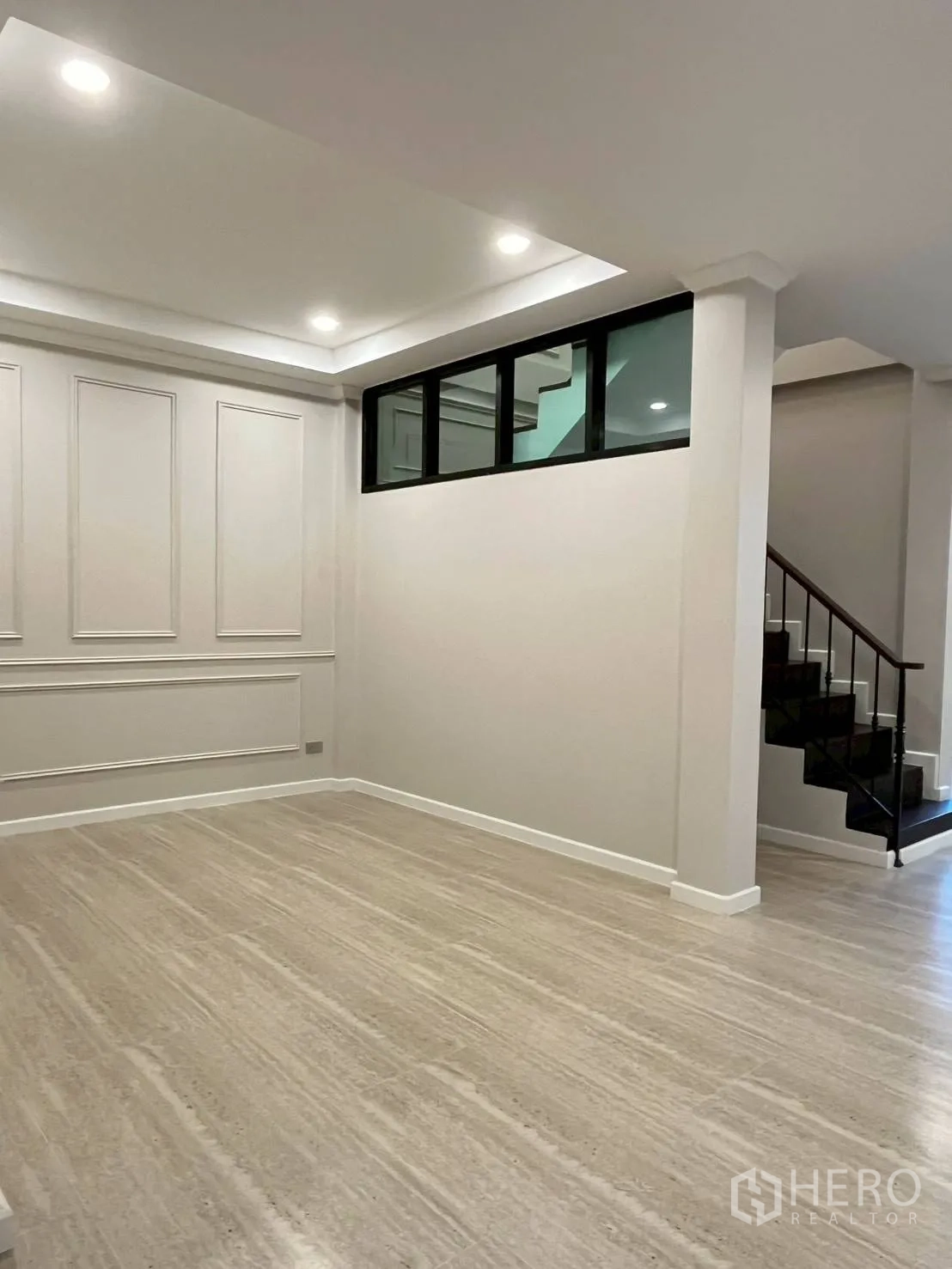 联排别墅 for rent in Khlong Toei, Bangkok - 开阔的起居区，嵌入式照明、墙面线条装饰、浅色地面与楼梯旁窗户。