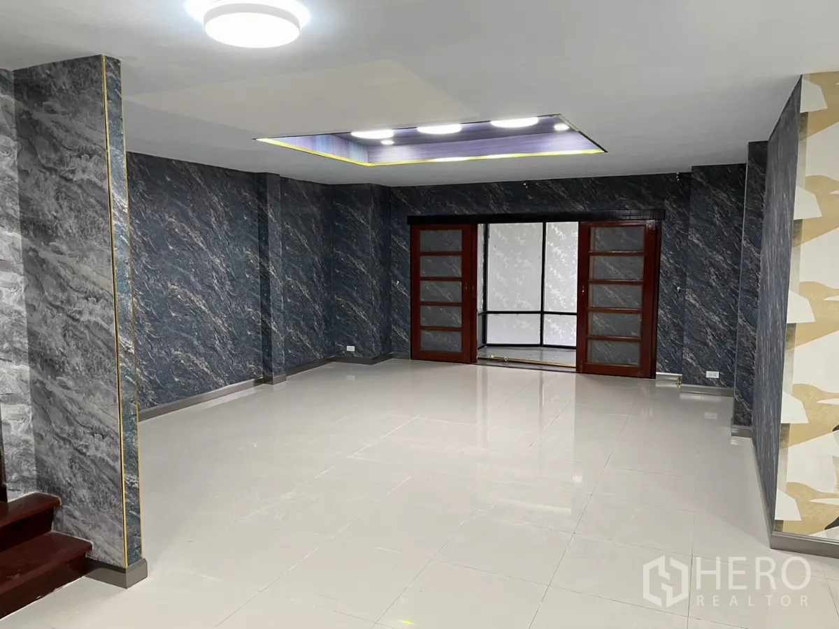 Detached House for rent in Watthana, Bangkok - Open living space with glossy tile floors and sliding doors to a glassed-in area.
