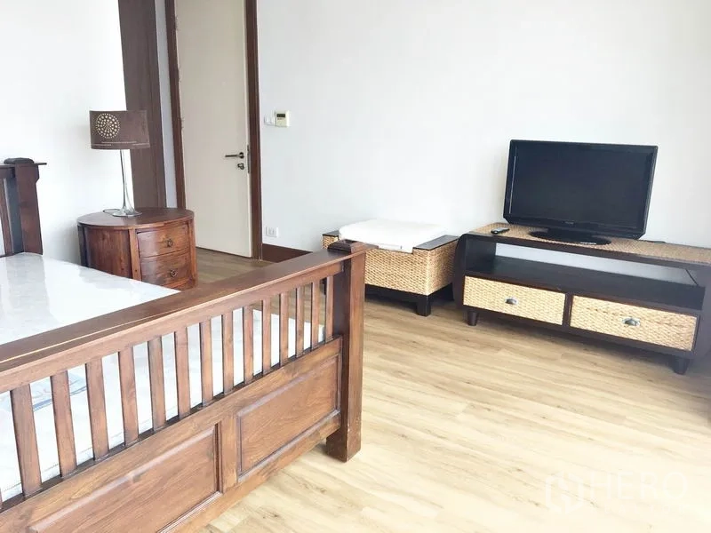 公寓 出租在Khlong Toei, Bangkok - 卧室一角，木床、电视柜与藤编抽屉，木地板。