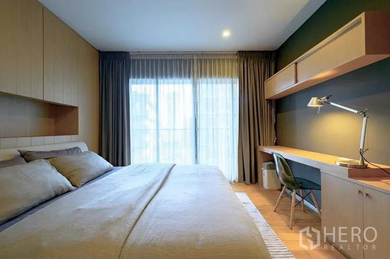 Condominium for rent in Watthana, Bangkok - Bright bedroom with king bed, full-height windows, built-in desk and shelving, and sheer curtains.