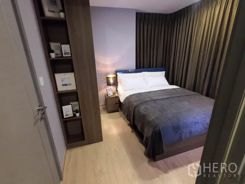 公寓 出租或出售在Watthana, Bangkok - 从入口望向卧室，可见木地板、收纳架与床头柜。