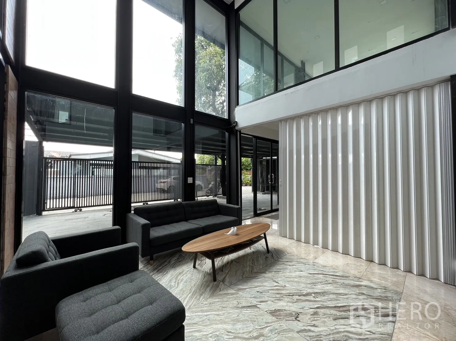 Detached House for rent or sale in Phra Khanong, Bangkok - Living room with mezzanine gallery and white folding wall panel beside tall glazing.