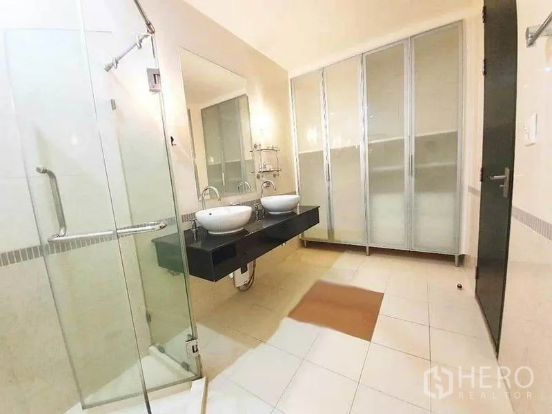公寓 出租在Ratchathewi, Bangkok - 宽敞浴室，玻璃淋浴间，黑色台面上的双台盆，配磨砂衣柜。
