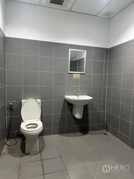 Factory for rent in Bang Sao Thong, Samut Prakan - Clean tiled restroom with toilet, wall-mounted sink, and mirror.