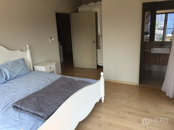 Condominium for rent or sale in Watthana, Bangkok - Spacious master bedroom with wood floors and an ensuite bathroom entrance in a modern Bangkok condo.