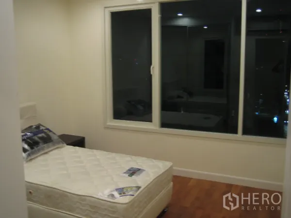 Condominium for rent or sale in Watthana, Bangkok - Second bedroom with single bed, bedside table, and a large window overlooking city lights.