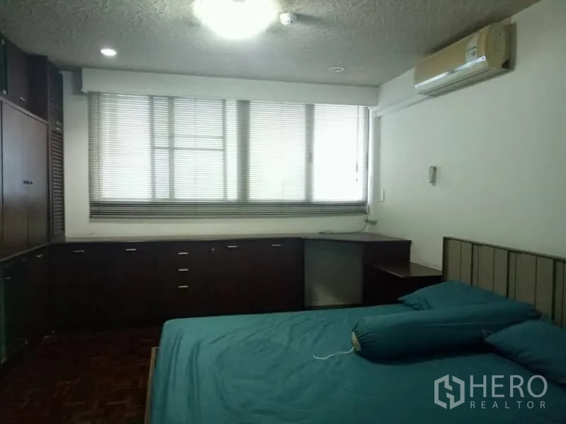 คอนโด ให้เช่าในWatthana, Bangkok - ห้องนอนที่สองพร้อมตู้บิวท์อินไม้เข้ม โต๊ะมุม มู่ลี่หน้าต่าง และเครื่องปรับอากาศติดผนัง