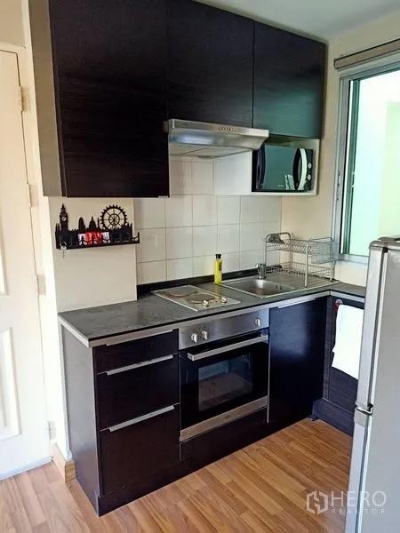 Condominium for rent in Khlong Toei, Bangkok - Close-up of kitchen featuring built-in oven, cooktop, hood and overhead cabinets by the window.