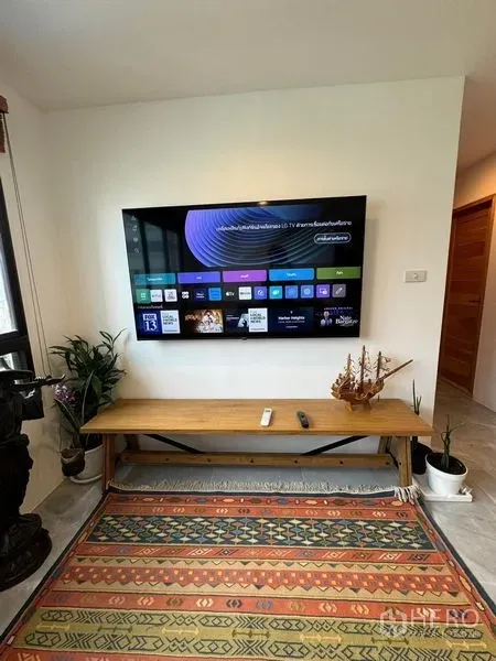 Condominium for rent or sale - Wall-mounted smart TV above a wooden bench with plants and decor in the living area.