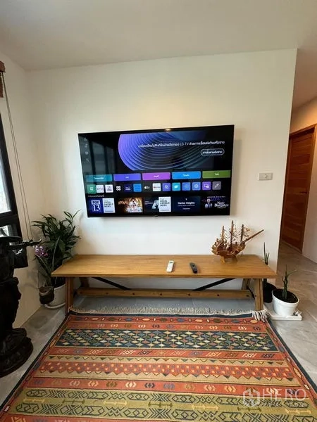 Condominium for rent or sale - Wall-mounted smart TV above a wooden bench with plants and decor in the living area.
