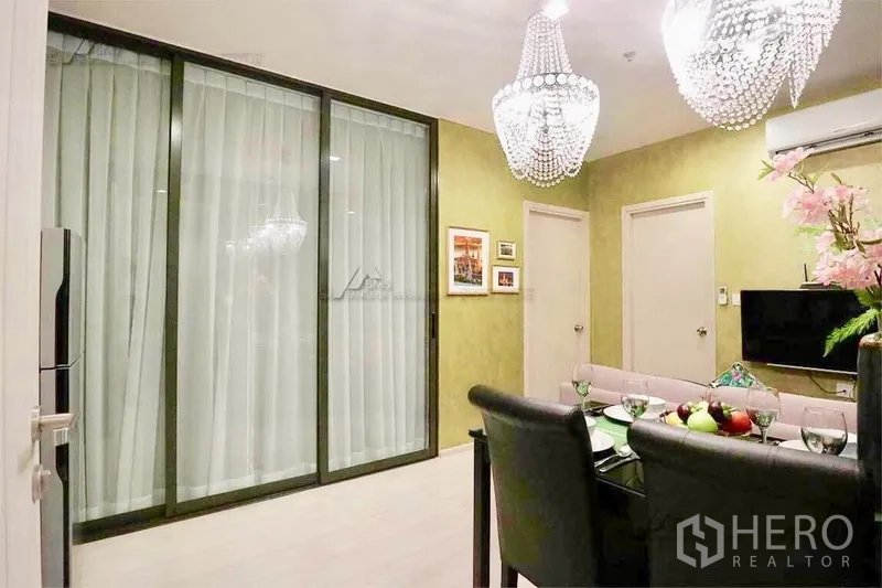 Condominium for rent in Khlong Toei, Bangkok - Dining area with large sliding glass partition, crystal chandeliers and wall-mounted TV.