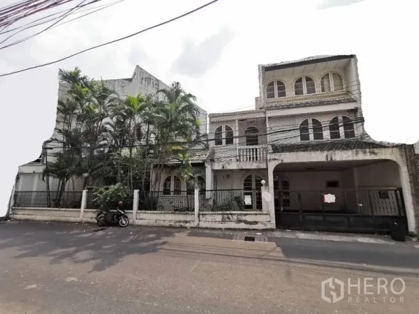 บ้าน ให้เช่าในKhlong Toei, Bangkok - มุมมองด้านหน้าบ้านเดี่ยวหลายชั้น หน้าต่างโค้ง มีระเบียง รั้วพร้อมที่จอดรถ และต้นปาล์มสูง ในเขตวัฒนา กรุงเทพฯ