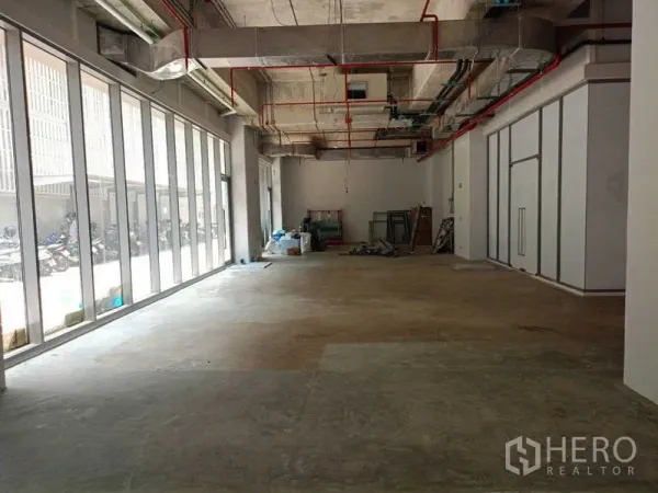 Retail Space for rent in Watthana, Bangkok - Open‑plan retail shell with floor‑to‑ceiling glass frontage, high exposed ceiling with red sprinkler pipes, and concrete floors ready for fit‑out.