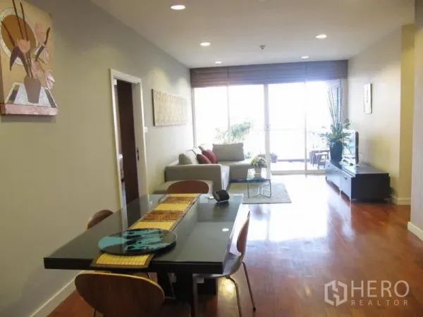 Condominium for rent in Khlong Toei, Bangkok - Spacious open-plan layout showing dining table, recessed lighting, and full-height windows to the balcony.