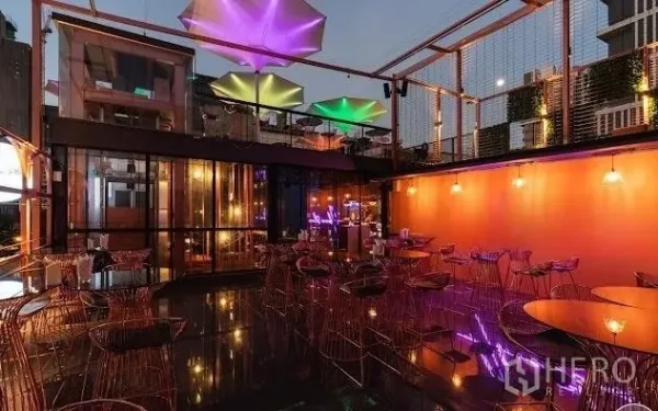 Retail Space for rent - Open-air rooftop terrace with wire-frame chairs, glass walls and colorful umbrella canopies at dusk.