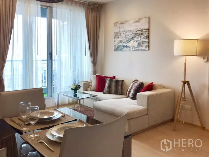 Condominium for rent in Khlong Toei, Bangkok - Bright living room with L-shaped sofa, dining set and floor-to-ceiling windows opening to a balcony city view.