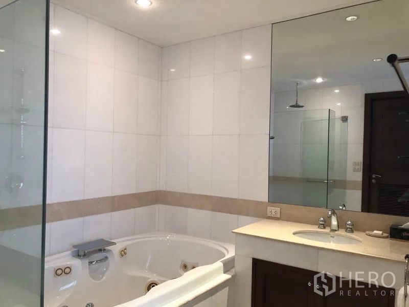 Condominium for rent or sale in Watthana, Bangkok - Modern bathroom with Jacuzzi bathtub, glass shower enclosure and wide vanity mirror.