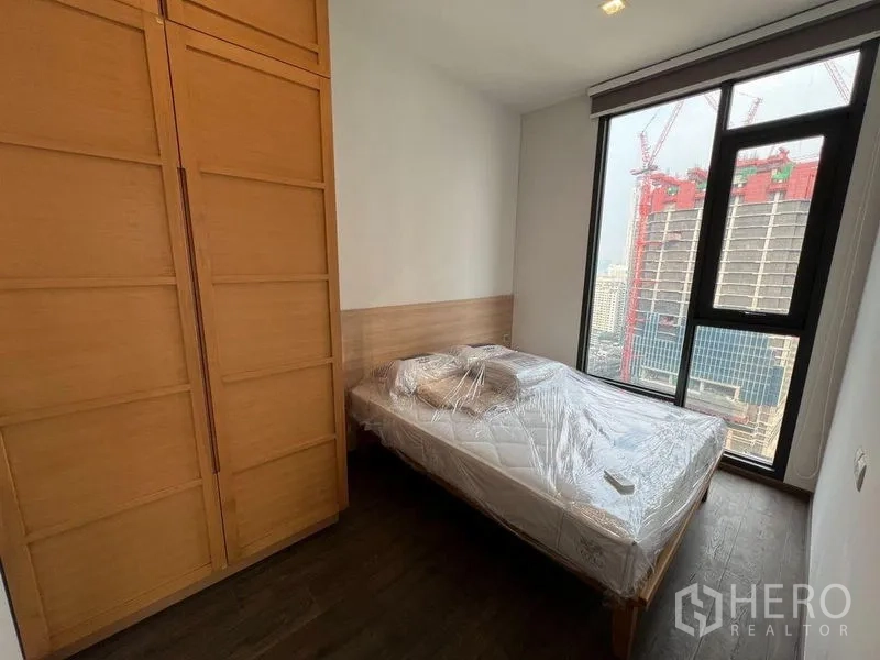 Condominium for rent in Ratchathewi, Bangkok - Second bedroom with wood wardrobe and city view window facing new construction.