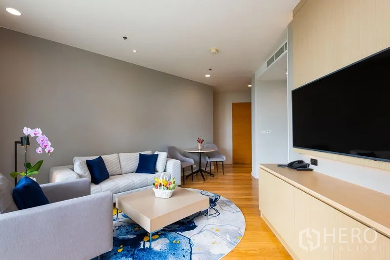 Condominium for rent in Bang Kho Laem, Bangkok - Modern living room featuring built-in TV wall, sofas, coffee table, and a small dining nook.