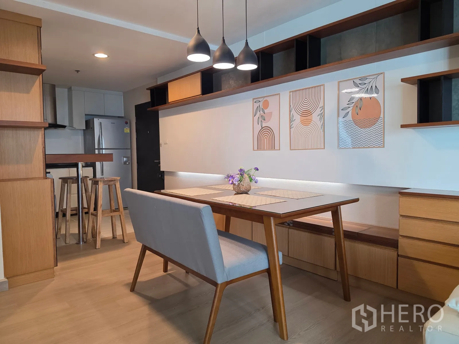 Condominium for rent in Huai Khwang, Bangkok - Dining space with wall art, long built-in shelves, and wood cabinetry.
