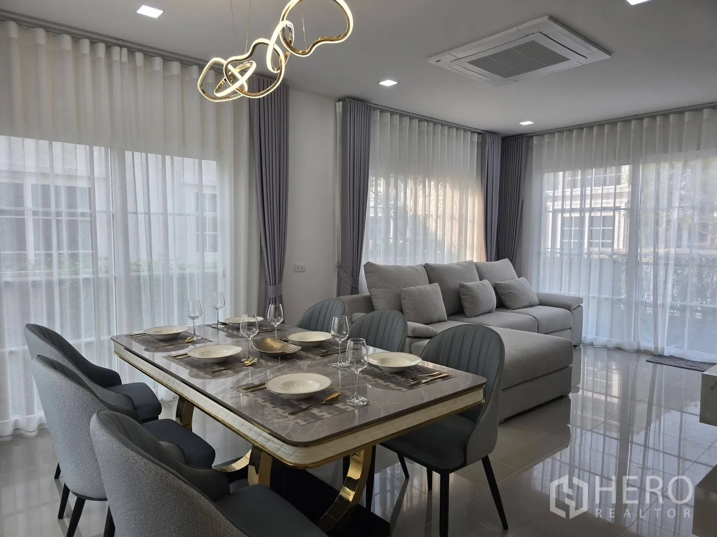 Semi-detached House for rent in Mueang Samut Prakan, Samut Prakan - Open-plan dining and lounge with marble-top table, modern gold chandelier and full-height windows.