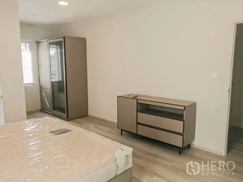 Townhouse for rent in Prawet, Bangkok - Spacious bedroom with wardrobe and low dresser against neutral walls and light-tone flooring.