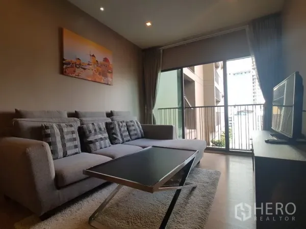 公寓 出租在Bangkok - 舒适客厅，转角沙发与茶几，大幅推拉门连接阳台。