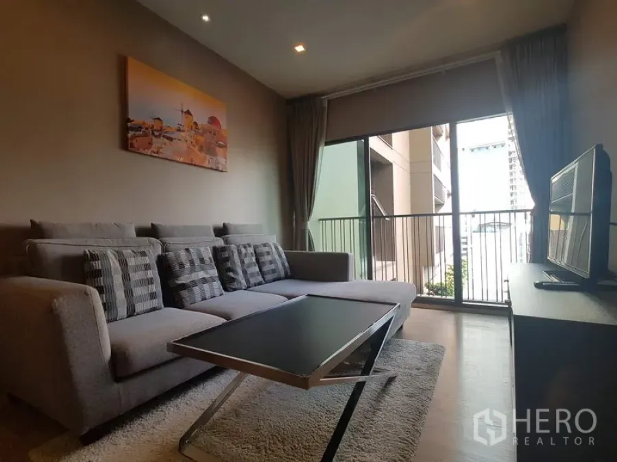 Condominium for rent in Bangkok - Cozy living room with sectional sofa, coffee table and large sliding doors opening to a balcony.