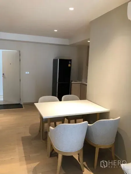 Condominium for rent in Watthana, Bangkok - Dining area with table and four upholstered chairs next to the open-plan kitchen and entry.