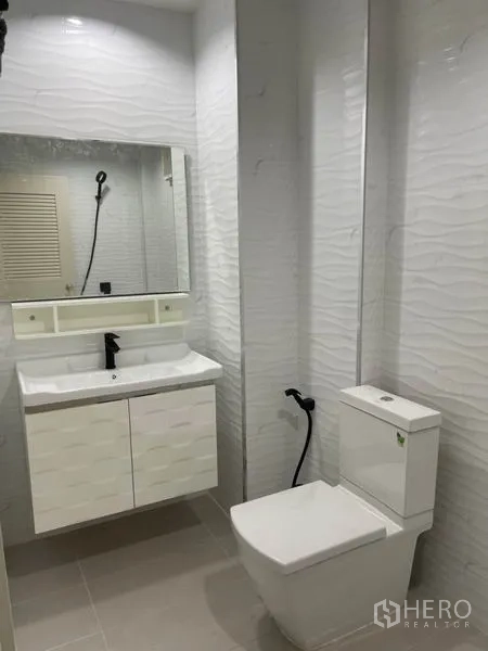 Townhouse for rent or sale in Yan Nawa, Bangkok - Modern bathroom with white textured tiles, vanity, mirror, and toilet.