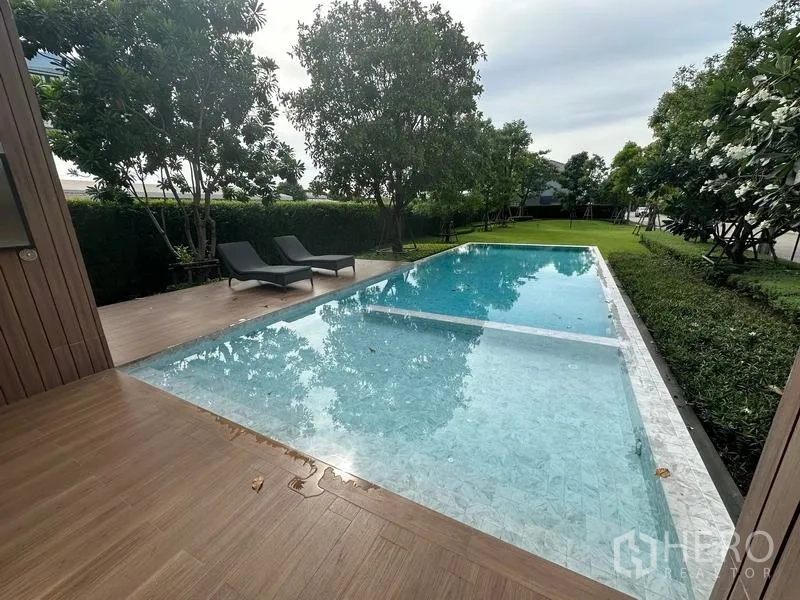 Detached House for sale in Nonthaburi - Resort-style shared swimming pool with sun deck, loungers and landscaped greenery.