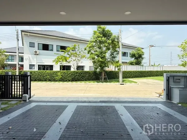 独立式住宅 出租在Bang Phli, Samut Prakan - 从有顶车库望向小区内道路与绿篱，前方无遮挡