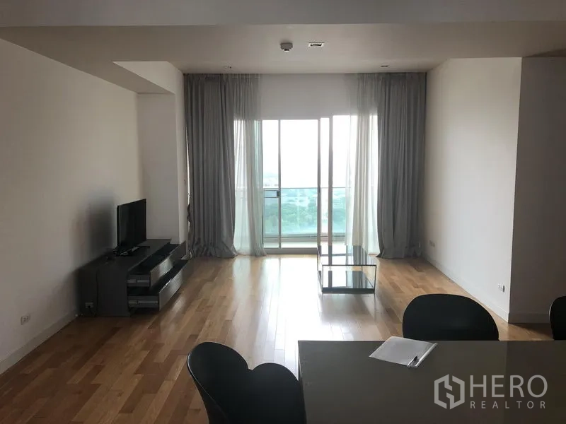 Condominium for rent in Khlong Toei, Bangkok - Bright living room with hardwood floors, TV console and balcony doors with sheer curtains in a Khlong Toei condo.