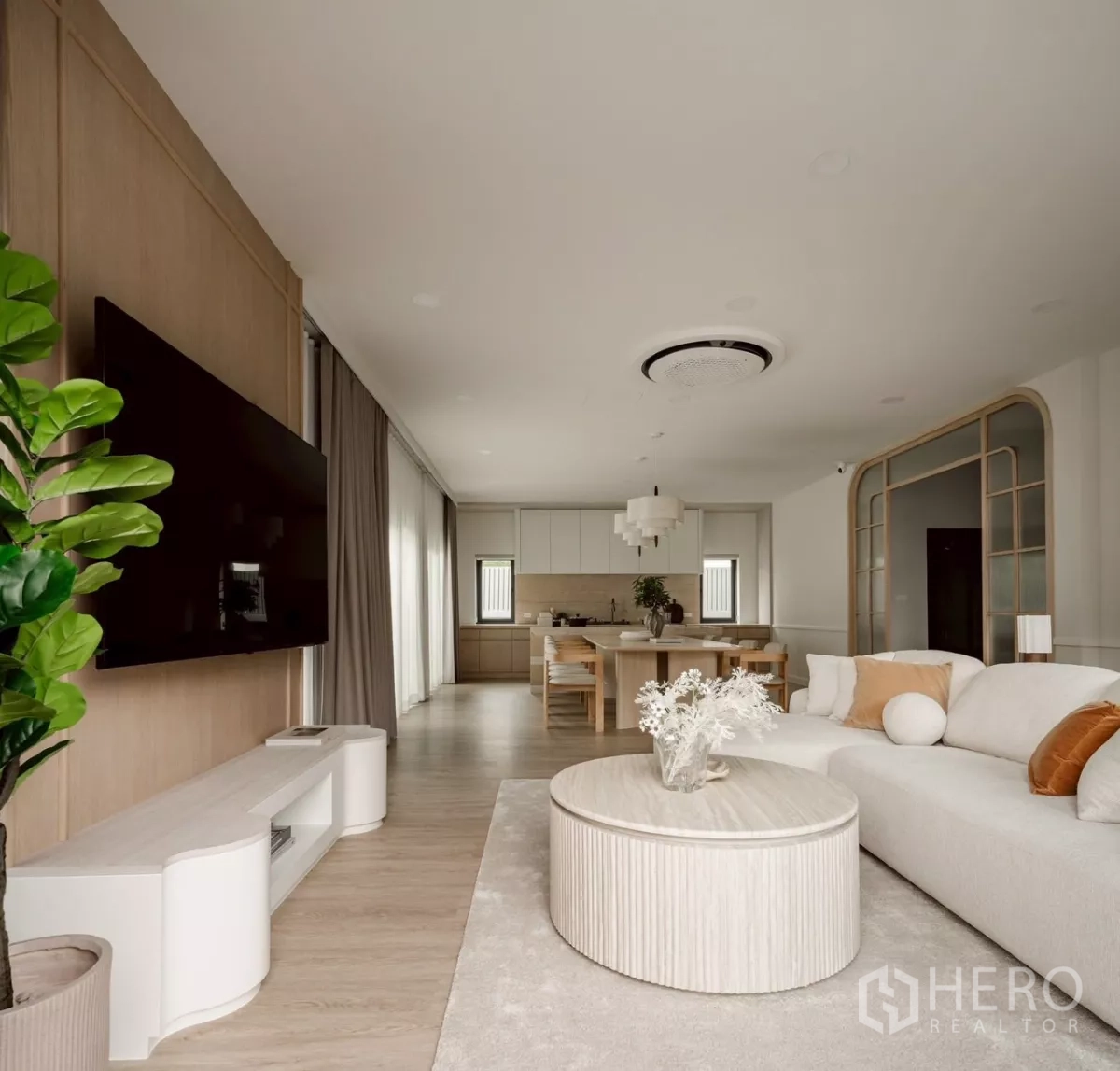 บ้าน ให้เช่าในBang Phli, Samut Prakan - ห้องนั่งเล่นแบบโอเพ่นพร้อมผนังทีวี โต๊ะกลางทรงกลม พื้นไม้โทนอ่อน และมองเห็นครัว–ทานข้าว