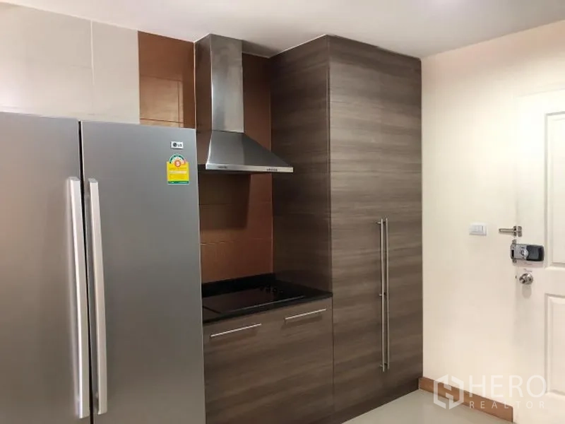 Condominium for rent in Khlong Toei, Bangkok - Kitchen corner featuring a large stainless fridge, cooktop with range hood, and tall pantry cabinet.