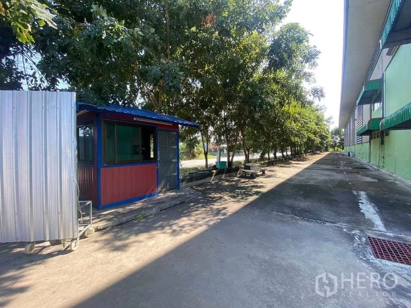 货栈 出租在Lat Lum Kaeo, Pathum Thani - 保安岗亭与树木成排的车道，毗邻仓库大楼。