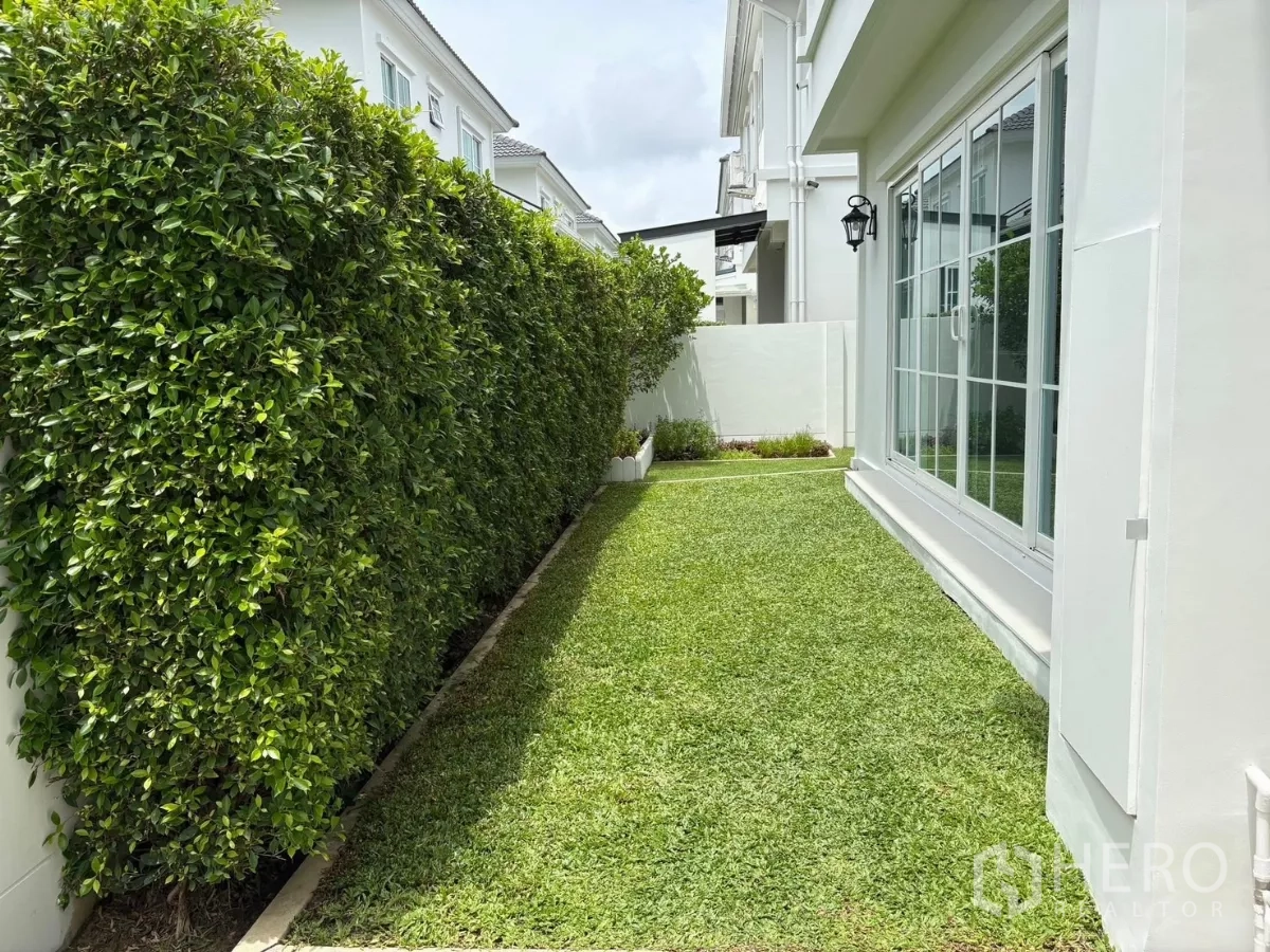 Detached House for rent or sale in Bang Phli, Samut Prakan - Narrow side yard with hedge privacy wall and sliding glass doors.