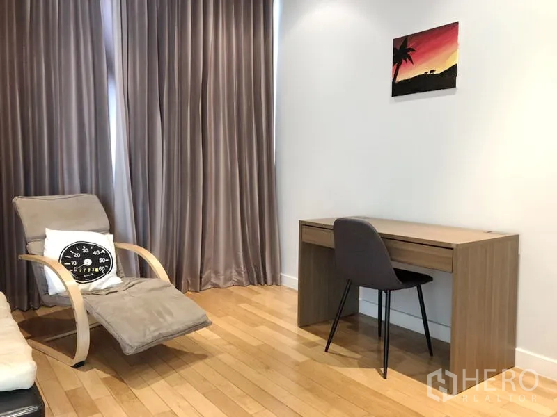 Condominium for rent in Khlong Toei, Bangkok - Secondary bedroom or study with lounge chair and work desk beside tall curtains.