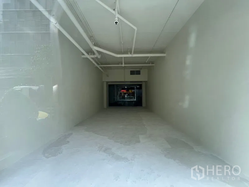 Retail Space for rent in Watthana, Bangkok - Long, narrow shop interior with exposed ceiling services and a glass door opening to the mall corridor.