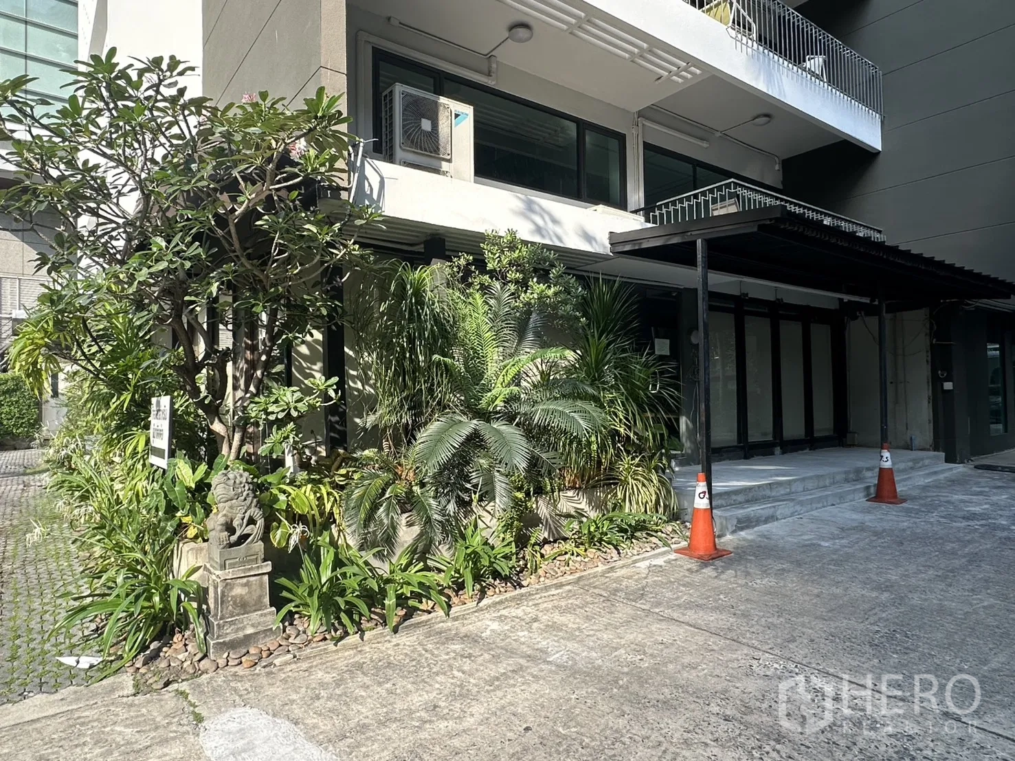 Retail Space for rent in Watthana, Bangkok - Shaded retail frontage with glass doors, black awning, and lush tropical landscaping by the entrance.