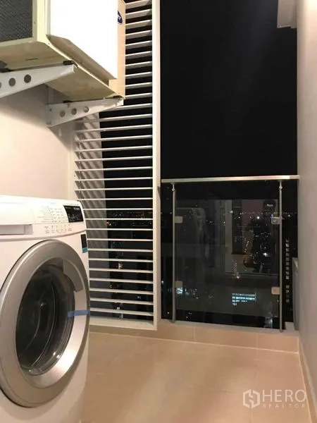 公寓 出租或出售在Ratchathewi, Bangkok - 半封闭阳台设洗衣机与百叶遮挡，玻璃栏杆外可见城市夜景。