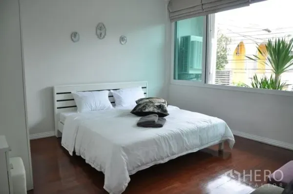 联排别墅 出租或出售在Watthana, Bangkok - 明亮卧室，双人床、白色墙面与木地板，旁有大窗户。