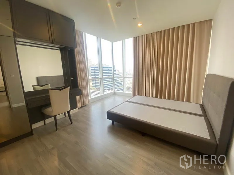 Condominium for rent in Bang Rak, Bangkok - Corner bedroom with dressing table and tall windows draped in beige curtains.