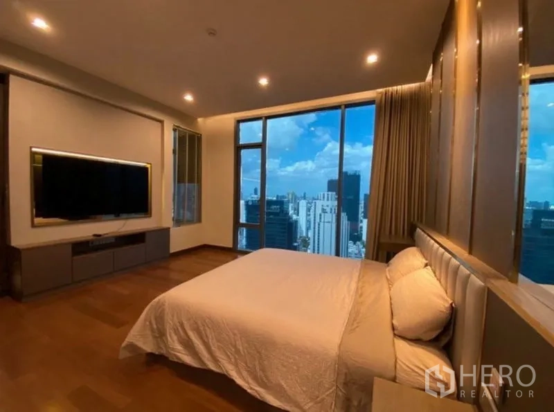 Condominium for rent in Khlong Toei, Bangkok - Master bedroom with panoramic city skyline views through tall windows and a mounted TV wall.