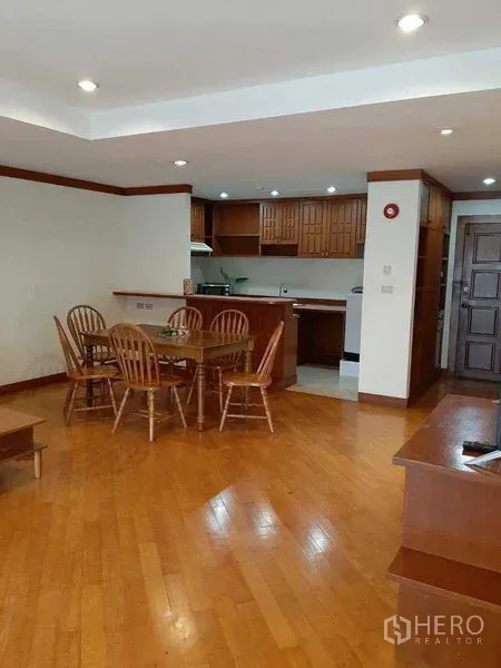 Apartment for rent in Watthana, Bangkok - Open kitchen with wooden cabinetry adjoining the dining area on hardwood flooring.